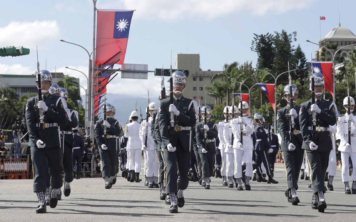 Troops in uniform and holding weapons march.