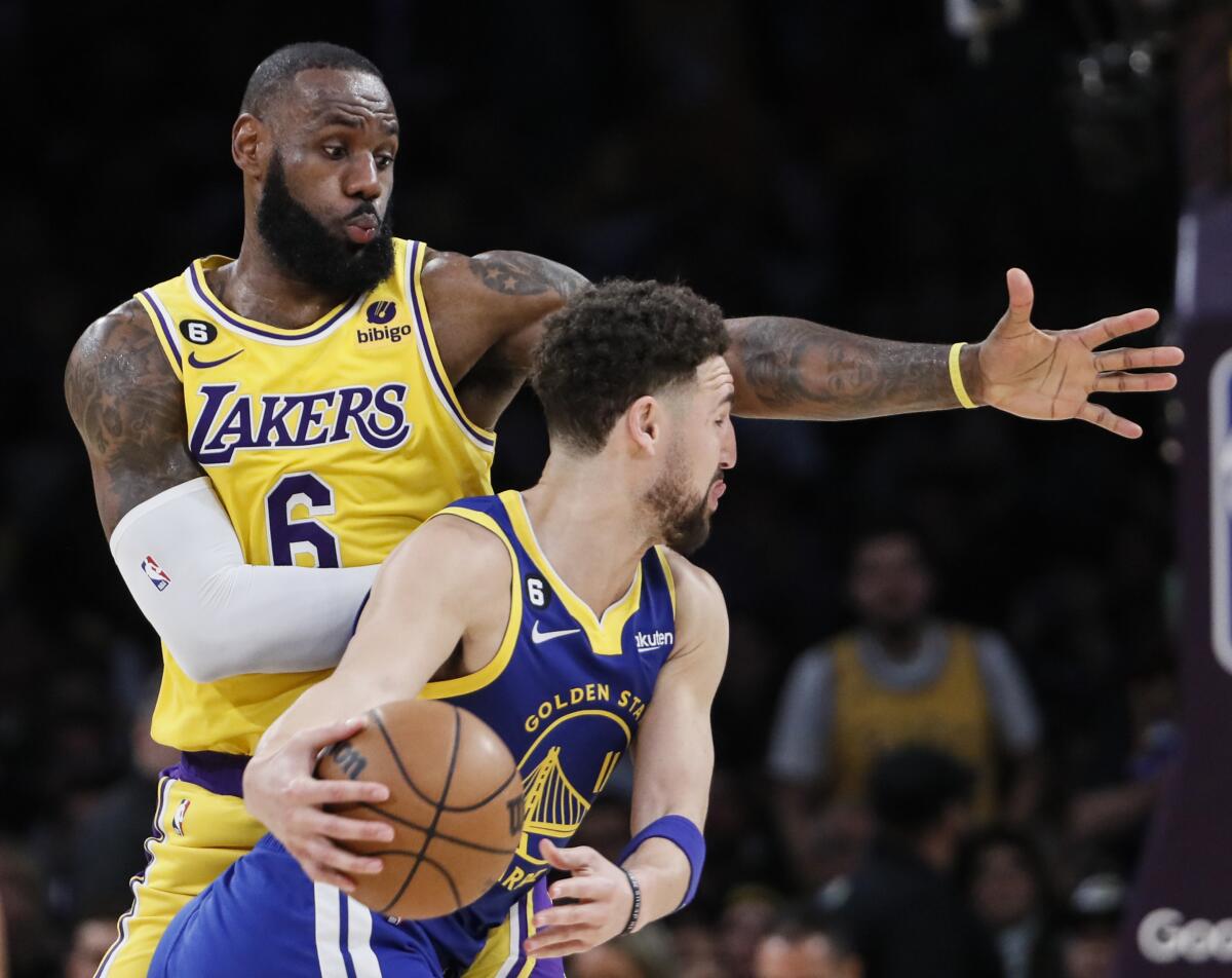 Lakers forward LeBron James, left, sticks out his left arm as Warriors guard Klay Thompson looks to pass as he drives.