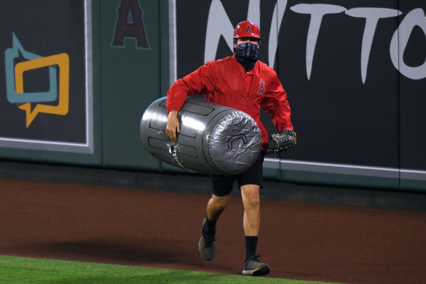 A member of the Angels grounds crew carries an inflated plastic trash can under his arm as he removes it from the field.