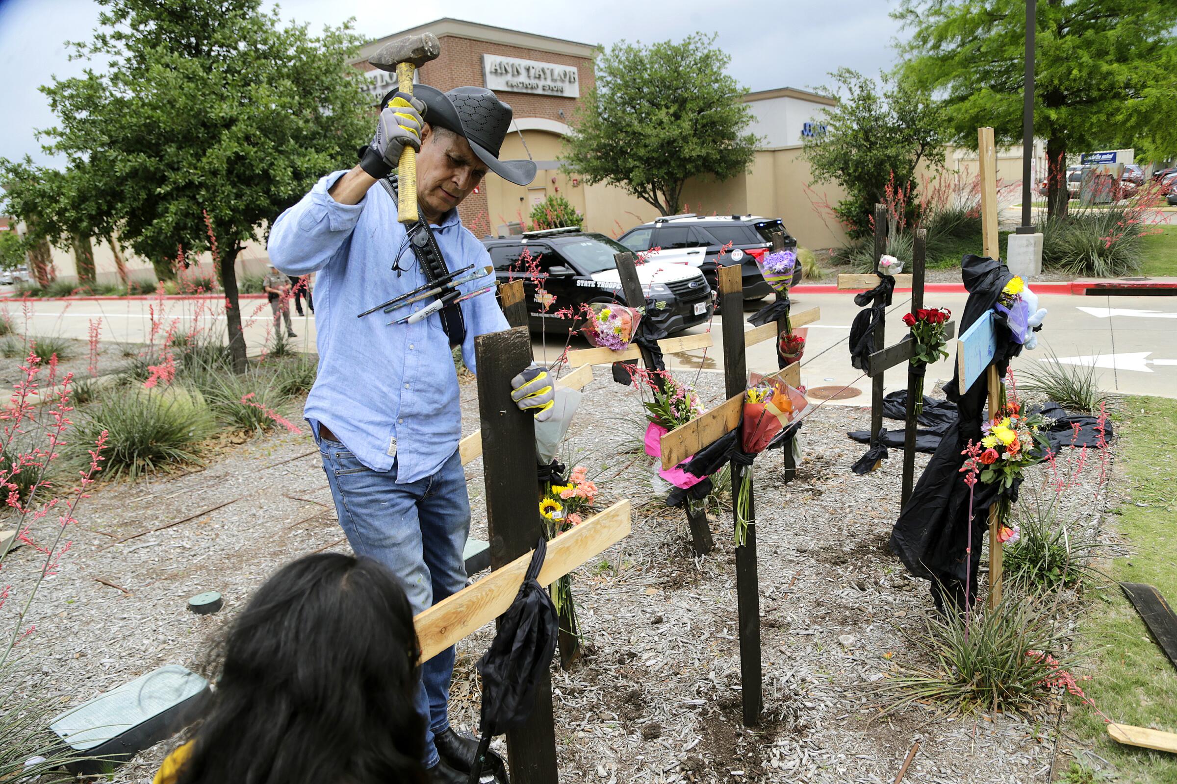 Roberto Marquez of Dallas constructs a memorial of wooden crosses near the scene of a mass shooting at an outlet mall.