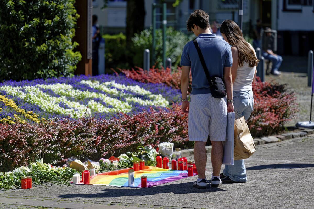 Two people stand facing a display of flowers and candles