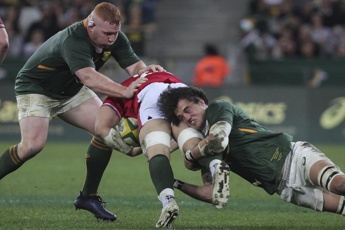 Damian de Allende of South Africa, right, tackles Josh Navidi of Wales while Steven Kitshoff of South Africa defends during the Rugby Championship test between South Africa and Wales in Cape Town, South Africa, Saturday, July 16, 2022. (AP Photo/Halden Krog)