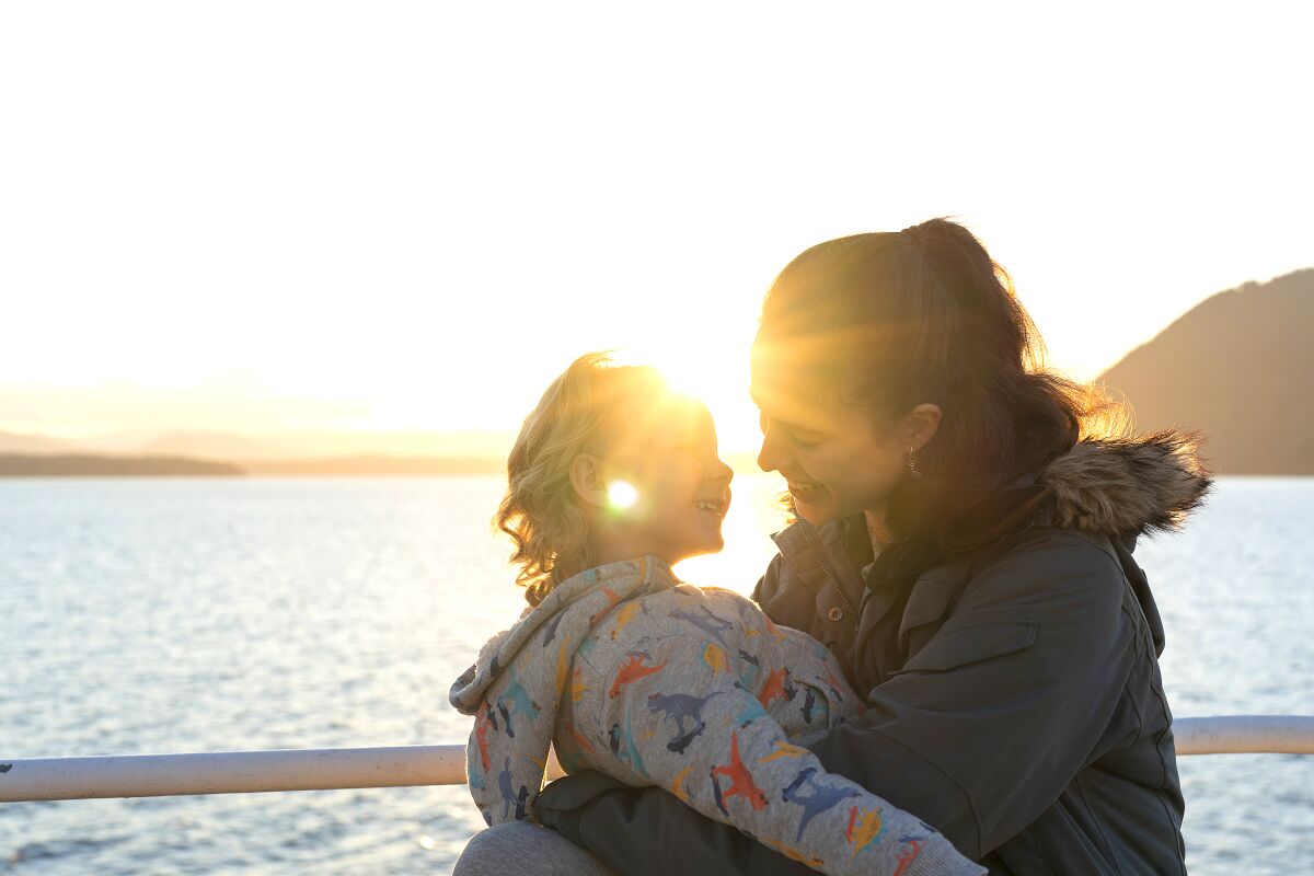 A mother holds her child with the setting sun behind them.