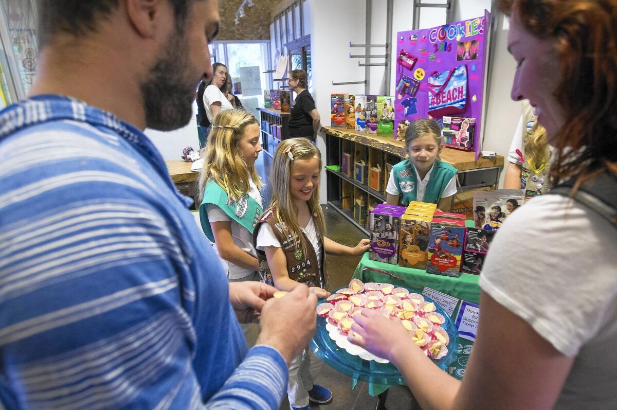 Kelly Richards, 9, center, with Taylor Mahan, 11, and Isabella Zuniga, 9, offers a sample to Michael Frank, left, and Kristi Drake while selling Girl Scout cookies at The OC Mix on Wednesday.