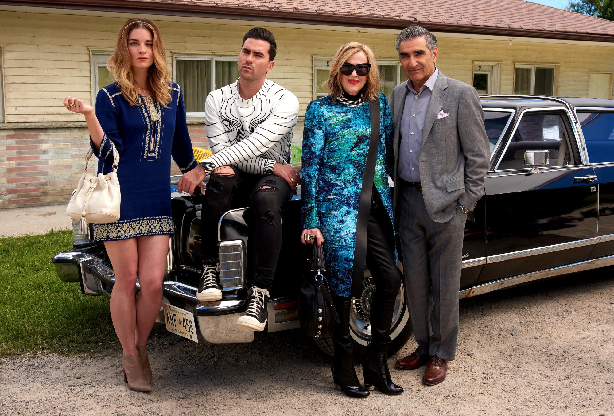 Four people leaning and sitting on top of an older model black car.