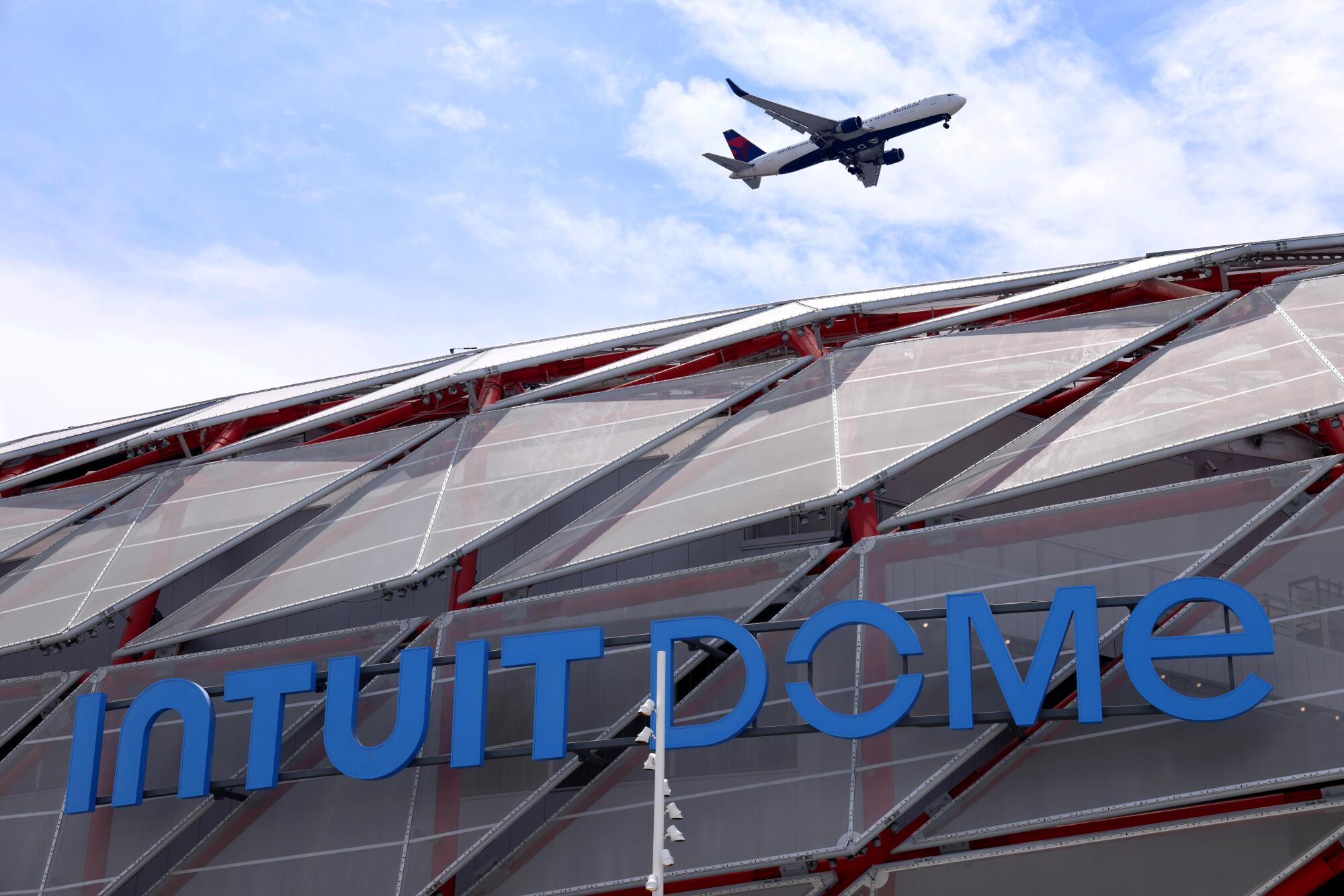 A plane flies over the new arena, whose blue letters spell out Intuit Dome.