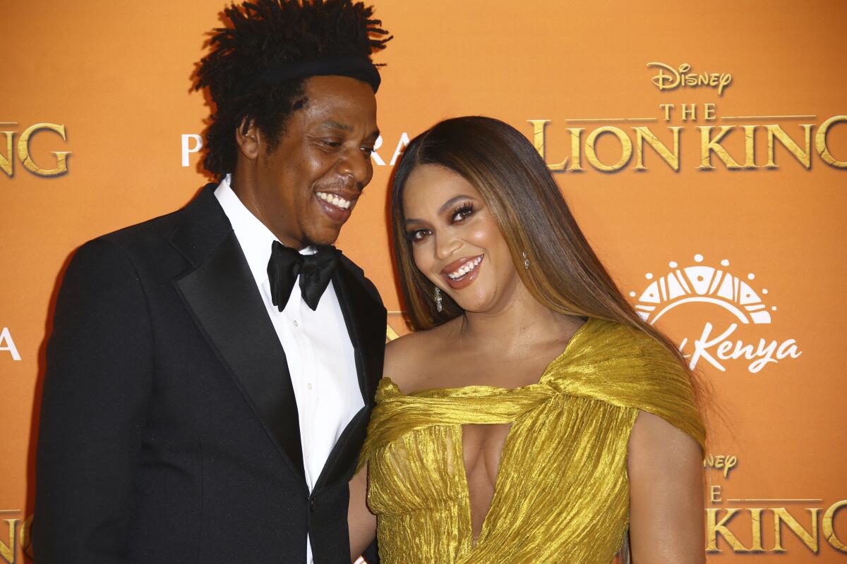 A man in a black tuxedo posing with and smiling at a woman in a gold dress who is also smiling
