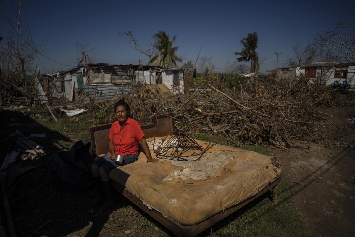 A woman sits on a bed outside her home