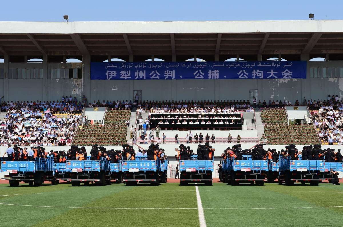 Security officers stand behind the accused, wearing orange vests and standing in trucks, during a mass sentencing in Yili prefecture in northwest China's Xinjiang region.
