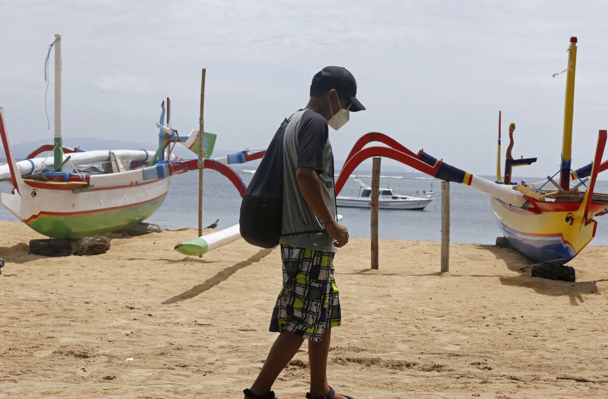 A man wearing a face mask to help curb the spread of coronavirus outbreak walks at a beach in Bali, Indonesia on Saturday, Dec. 5, 2020. (AP Photo/Firdia Lisnawati)