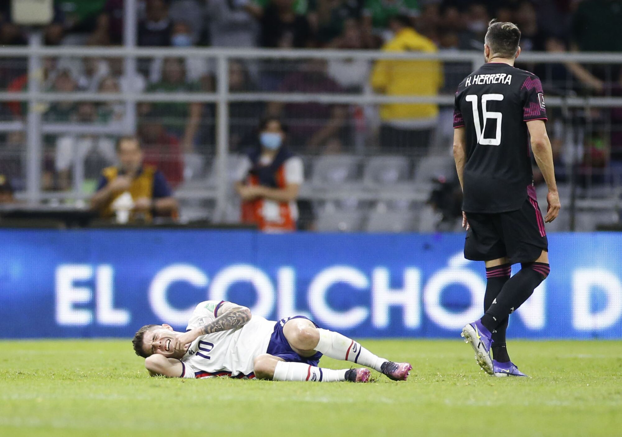 U.S. forward Christian Pulisic grimaces after being taken down as Mexico defender Hector Moreno walks next to him.