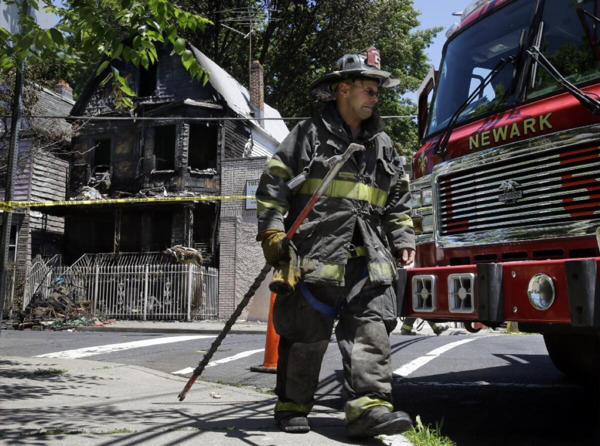 A firefighter walks outside the site of a Sunday-morning fire in Newark, N.J., that killed six people.