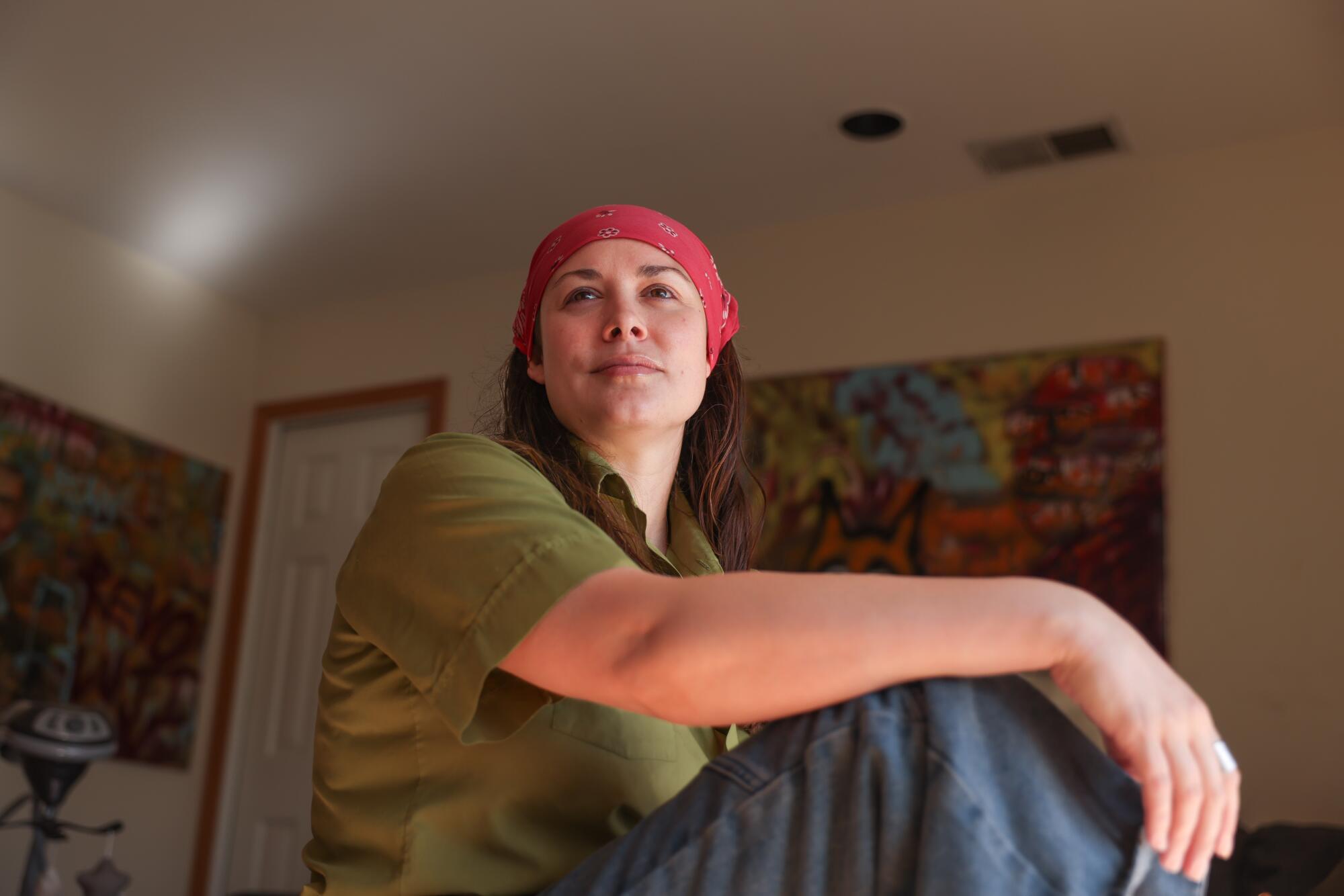 A woman wearing a bandana sits with her arm resting on her knee.