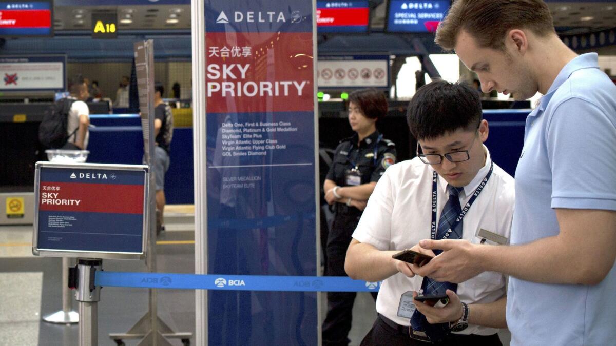 A Delta Air Lines employee assists a passenger near the check-in counters for Delta Air Lines at Beijing Capital International Airport in China. The carrier announced a new boarding process that begins Jan. 23.