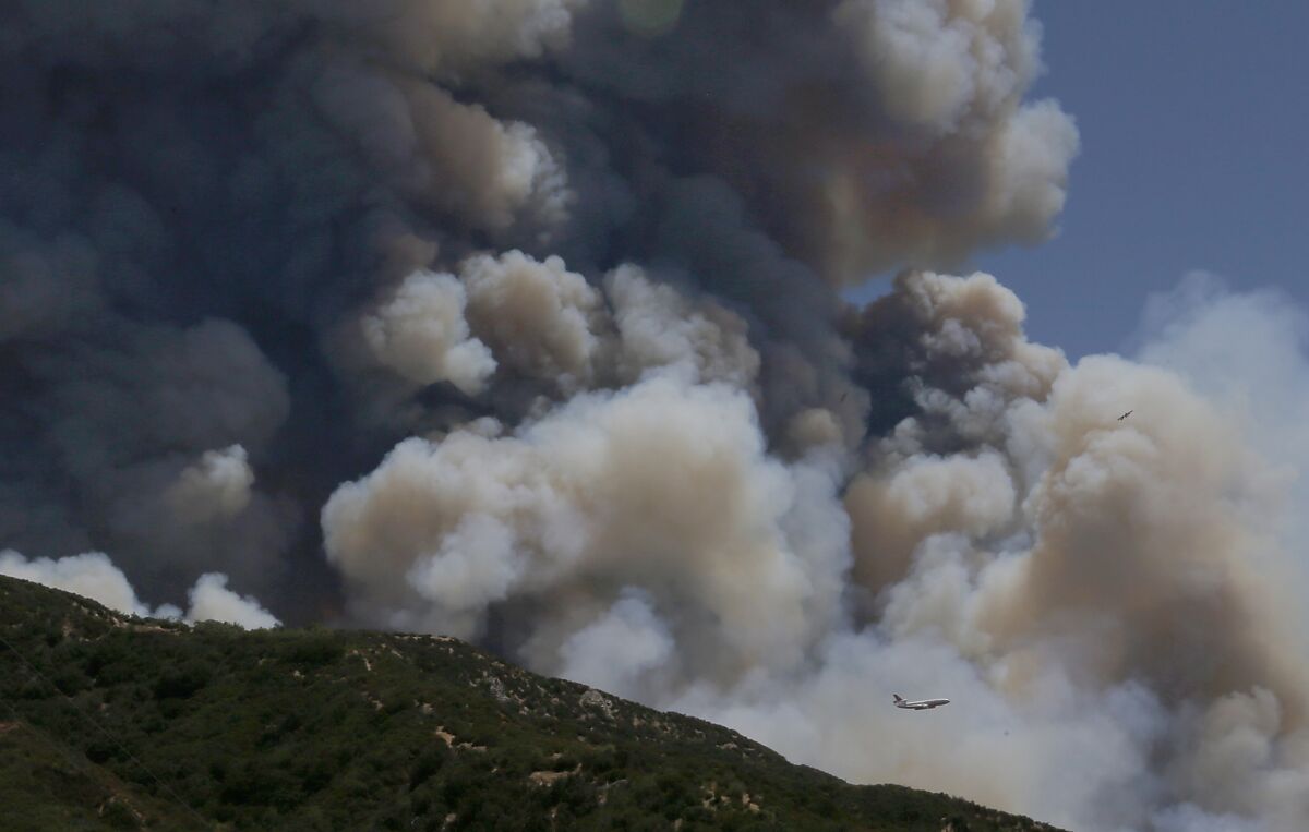A firefighting jumbo jet is dwarfed by the smoke from the Apple fire in the hills above Beaumont.
