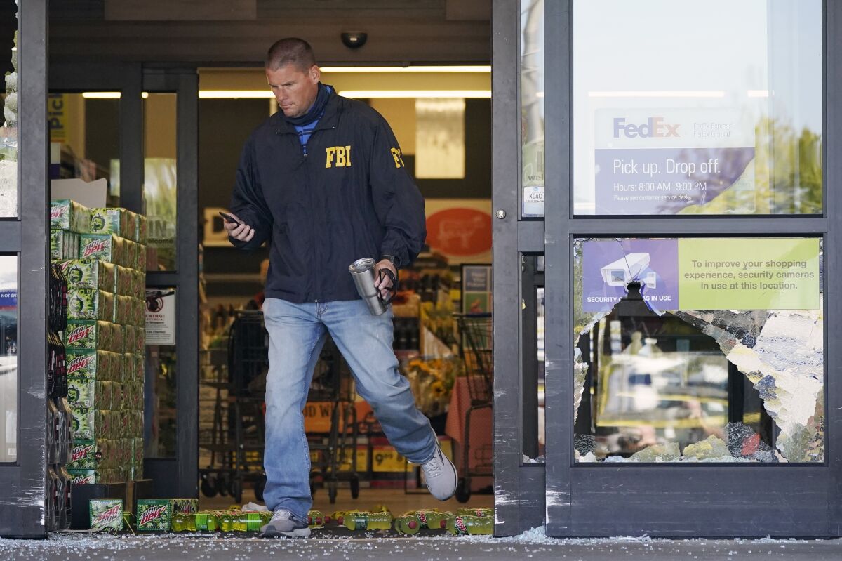An FBI agent steps over soft drink bottles and broken glass as he walks through a damaged store entrance.