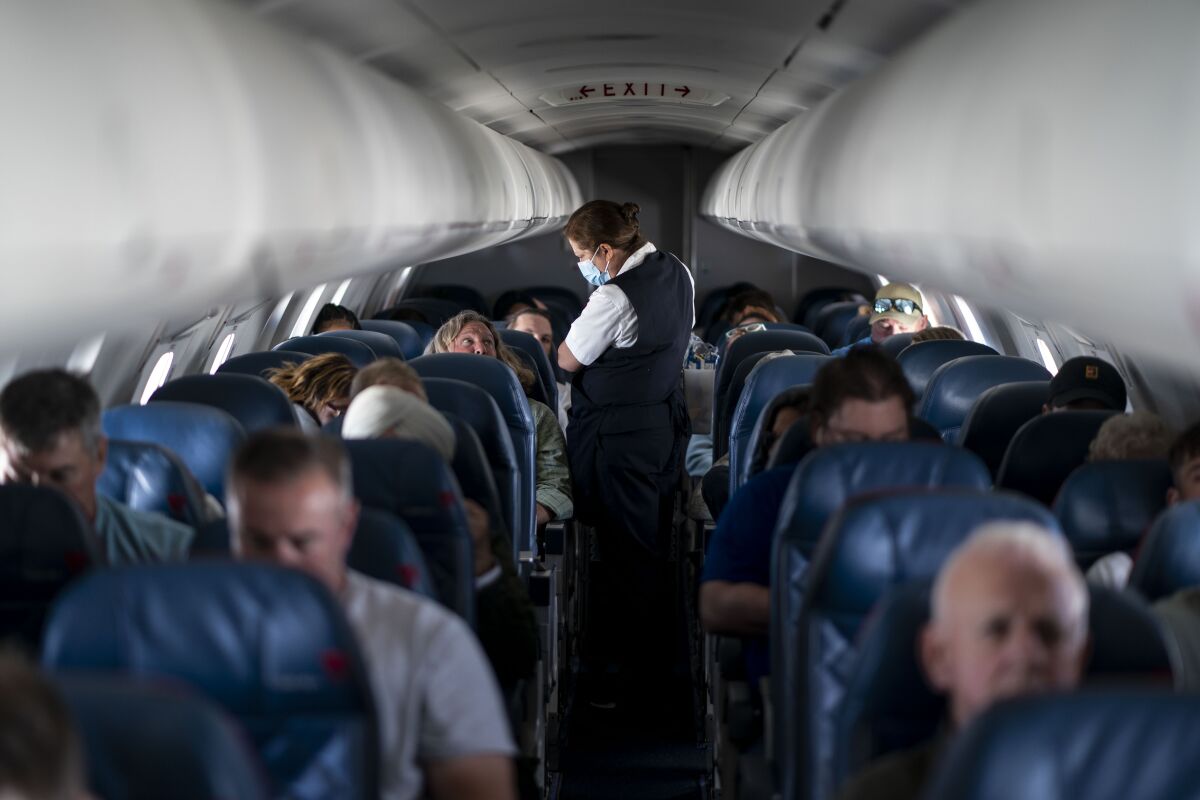 A flight attendant stands in the aisle of a plane filled with passengers