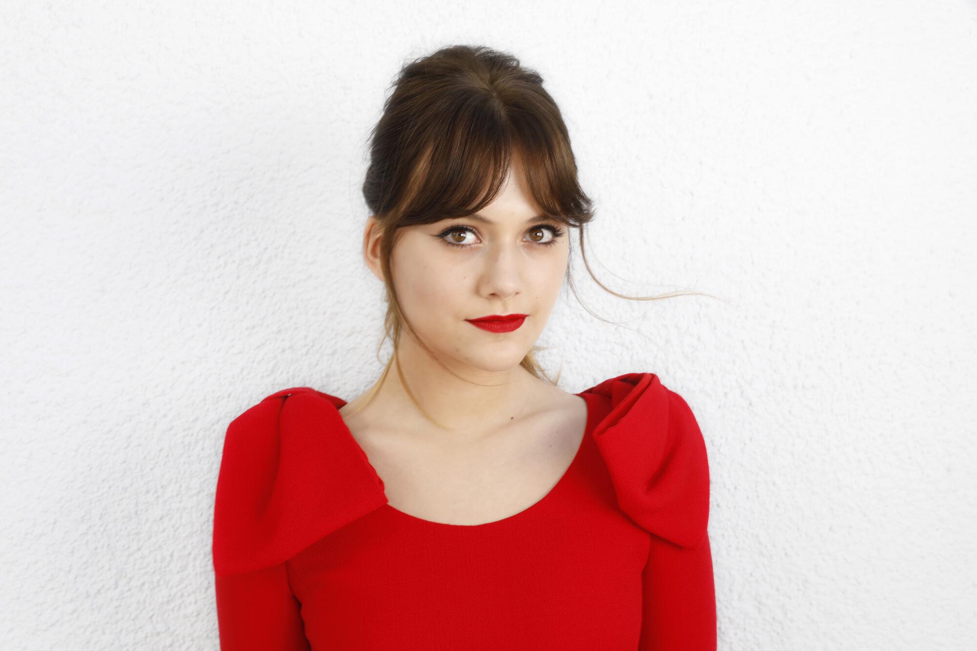 A young woman in a red dress looks at the camera