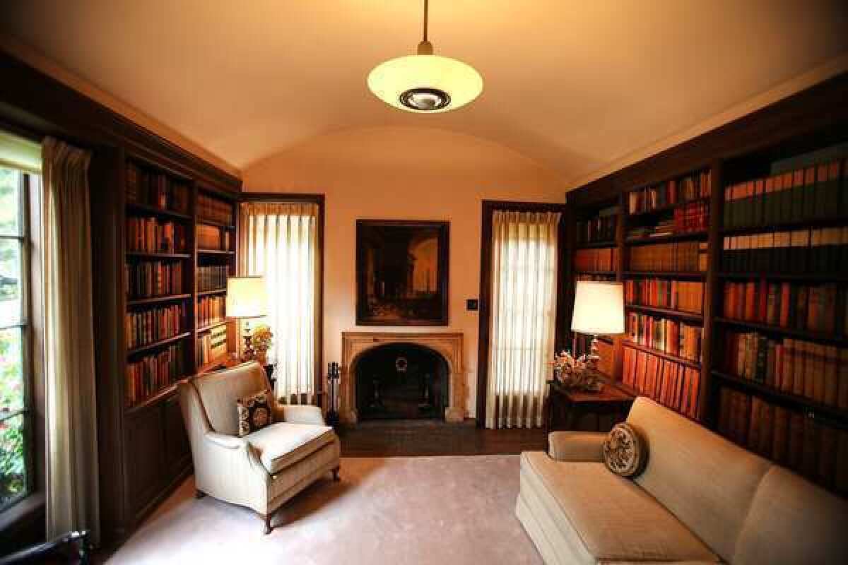 Wood bookshelves, detailed in the Winter House's original blueprints, line either side of the barrel-ceilinged library, and a fireplace with a tile-surround is flanked by tall windows.