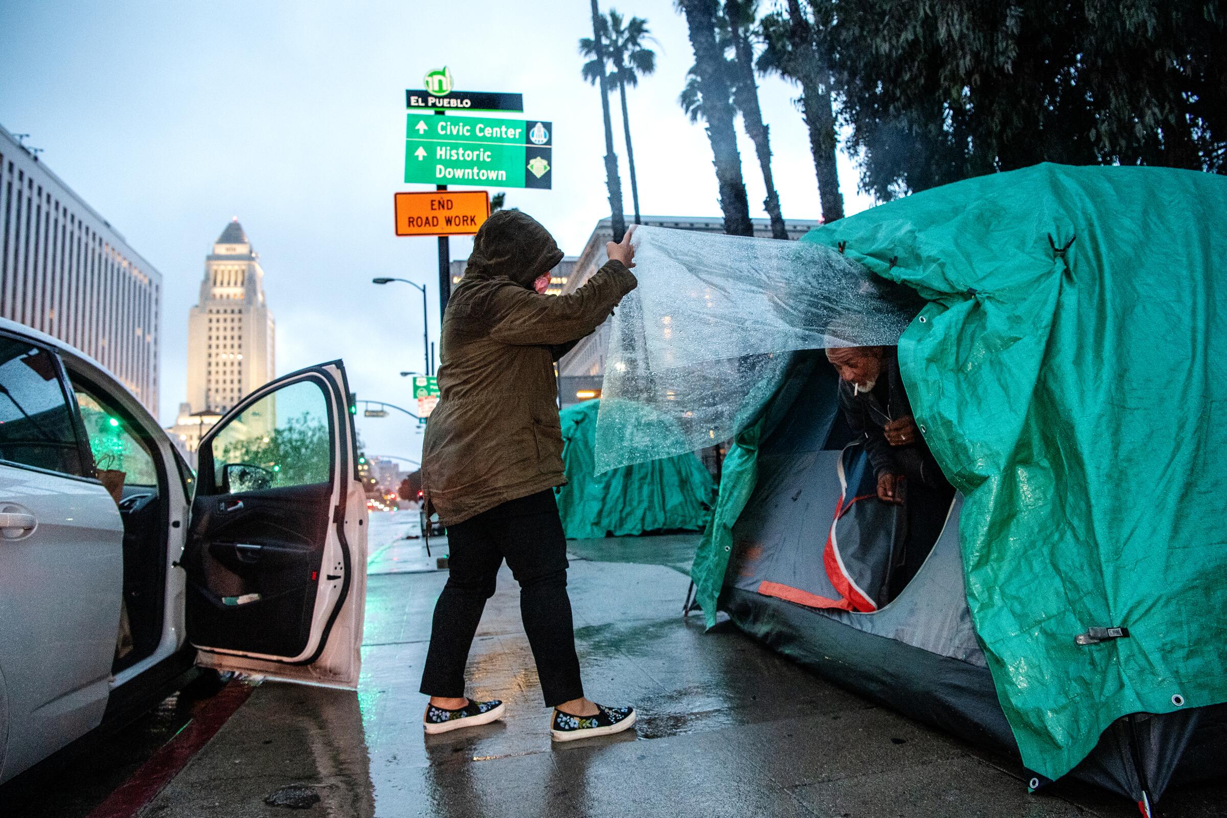 Melissa Acedera distributes meals and supplies to one of her contacts, Harvey, on Olvera Street on a rainy evening in downtown Los Angeles.