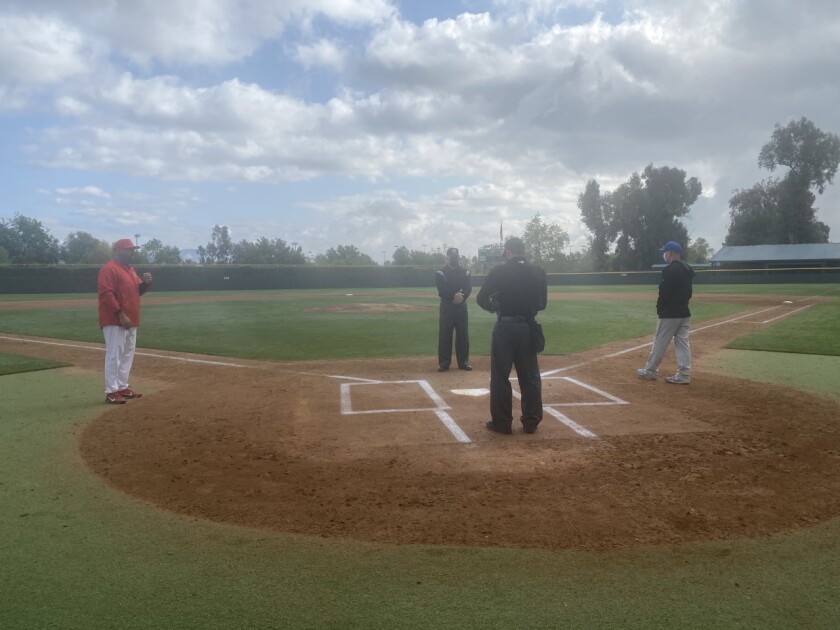 Coaches and umpires stand several feet apart around home plate