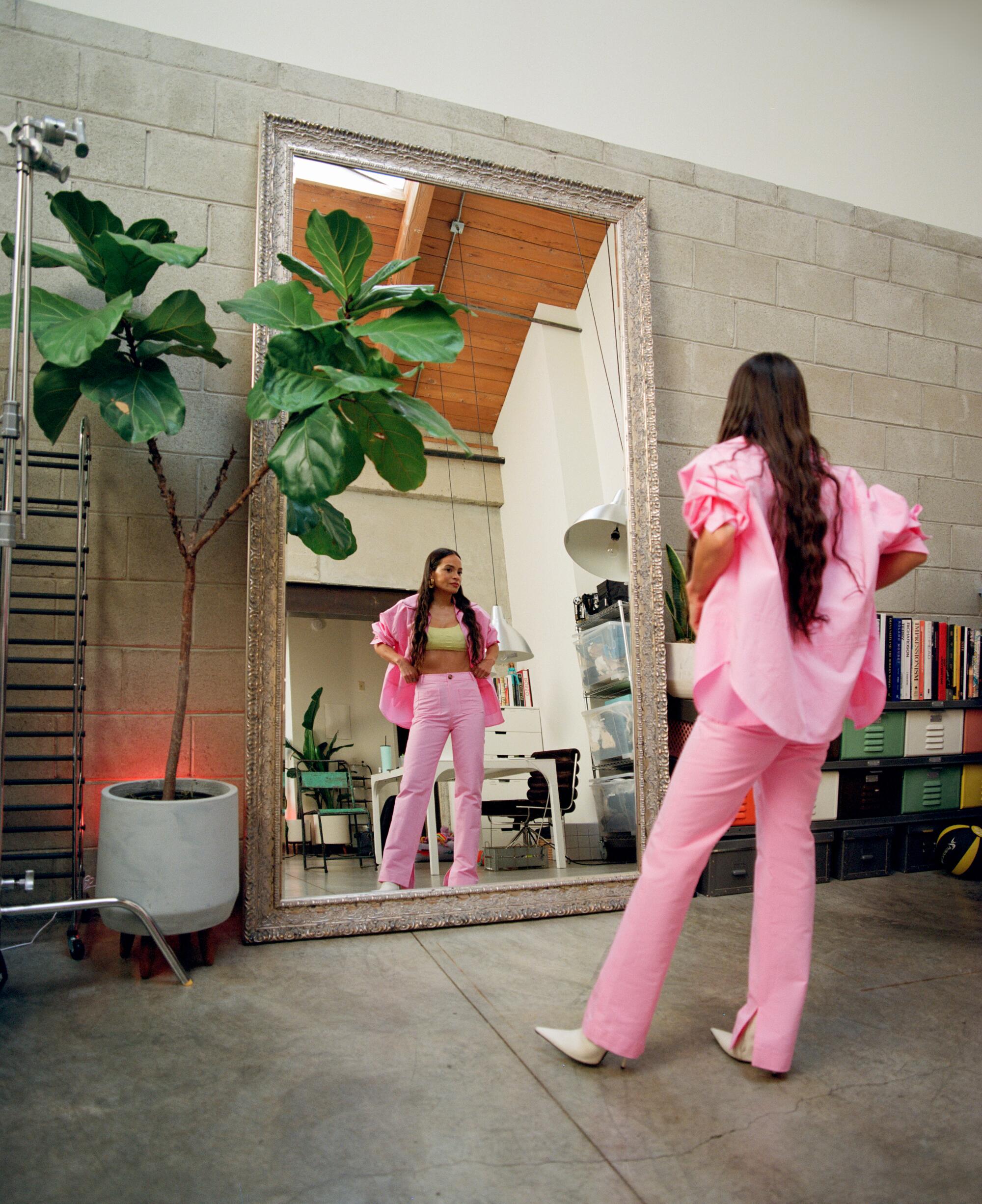 A woman in a pink jacket and pants looks at herself in a large mirror.