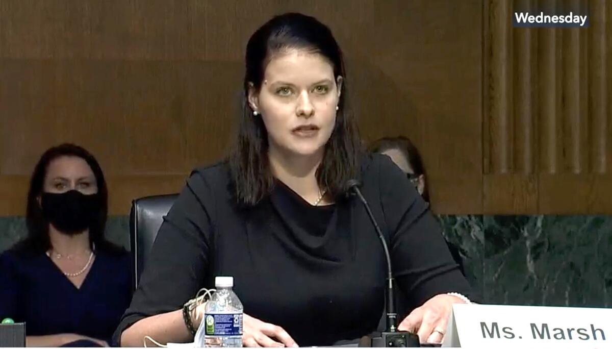 Amy Marsh sits and speaks into a microphone in a hearing room. 