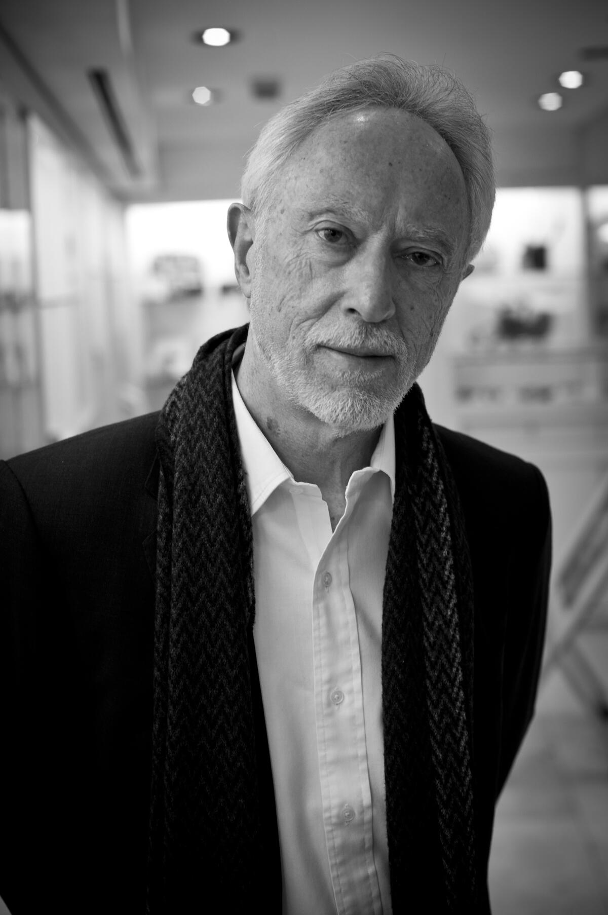 An older man standing in a dark jacket and white dress shirt in black and white.