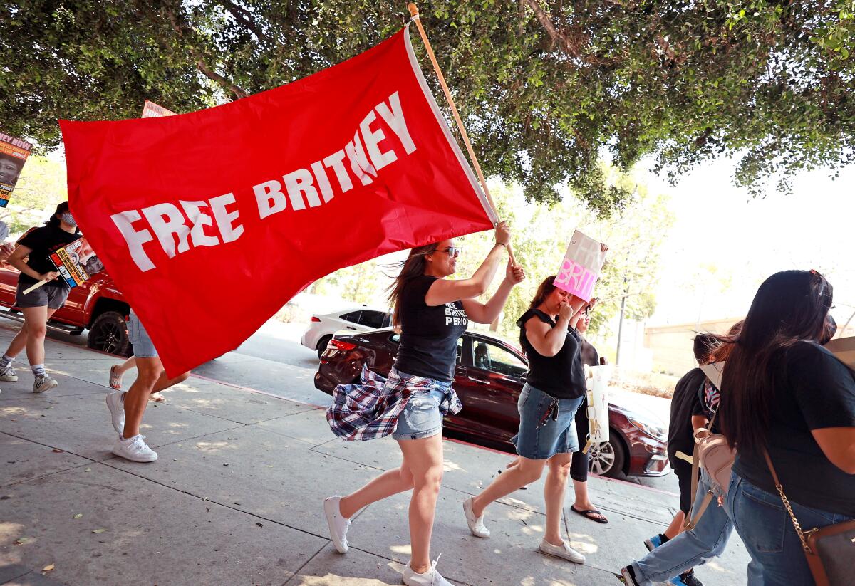 A young woman walks in the street carrying a red Free Britney flag