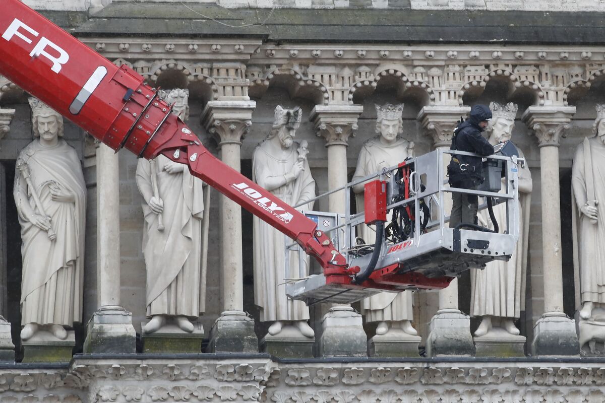 A crane carries a worker in front of statues adorning the cathedral.