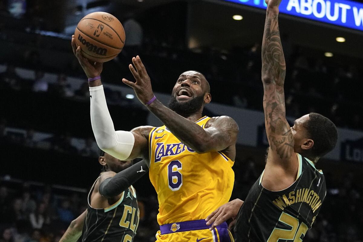 Lakers forward LeBron James splits the defense of Hornets forwards Jalen McDaniels, left, and P.J. Washington.