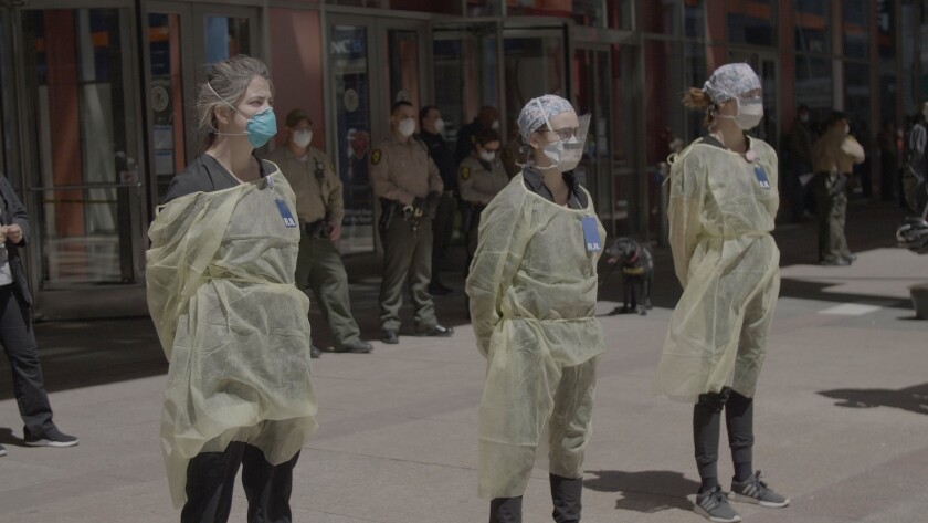 Three people in hospital-working gear stand outside with their hands behind their back