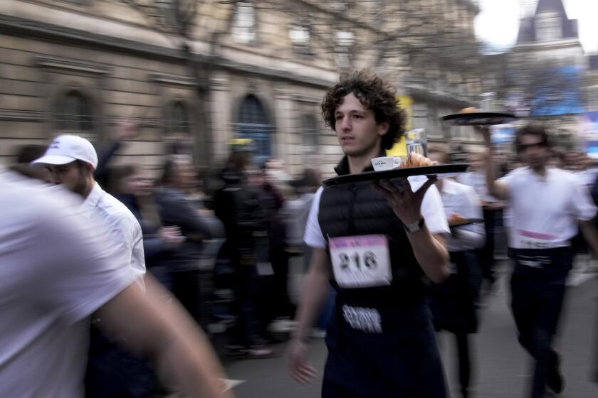 Waiters carry trays with a cup of coffee, a croissant and a glass of water as they take part in a waiter's run through the streets of Paris, Sunday, March 24, 2024. (AP Photo/Christophe Ena)