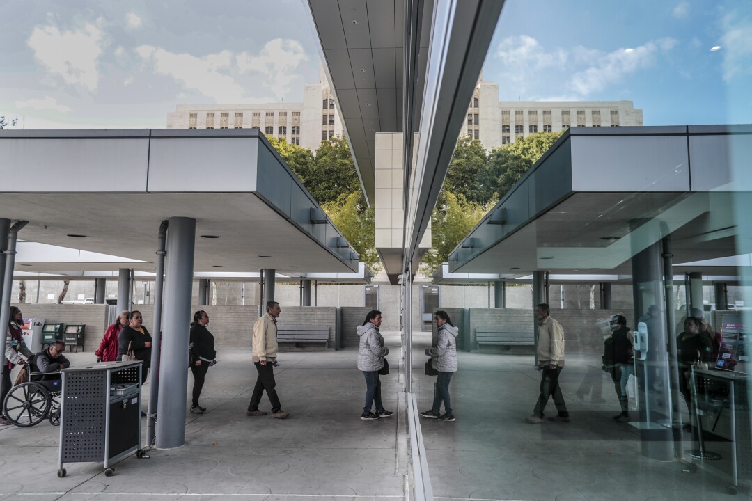 People waiting in line are reflected in the glass windows of a hospital building