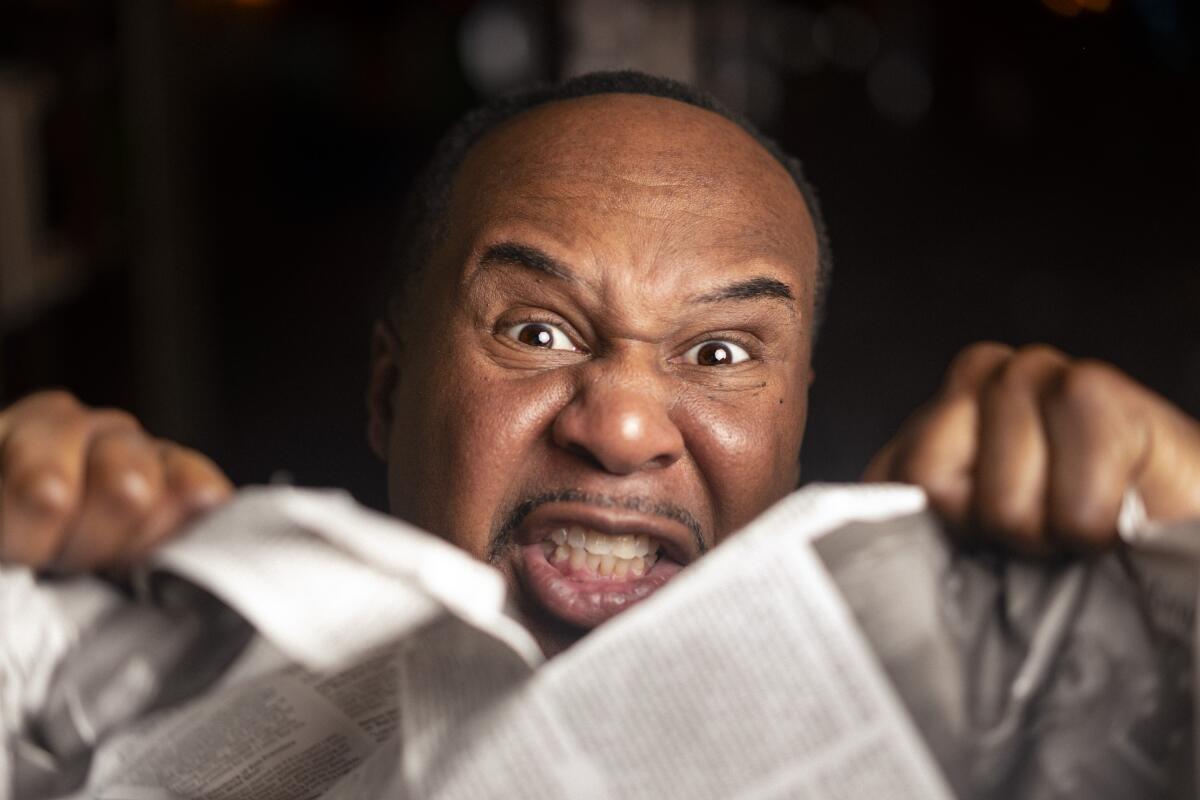 A close-up of a man's face grimacing and tearing a newspaper in two.