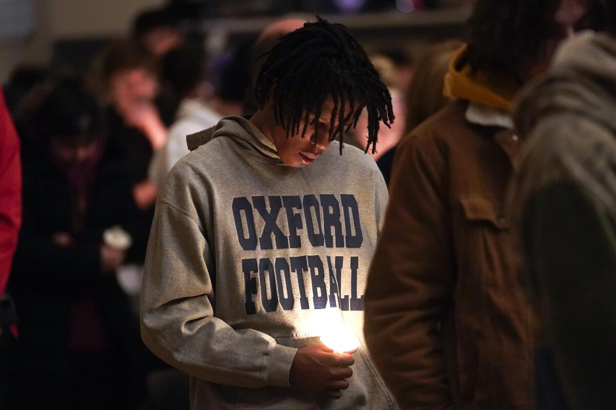 A person in an Oxford Football hoodie bows his head over a candle at a vigil.