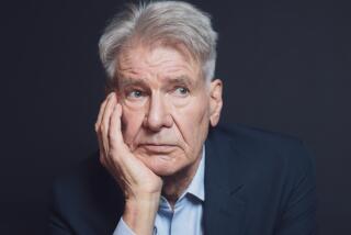 Harrison Ford holds one hand to his face and leans against a stool.