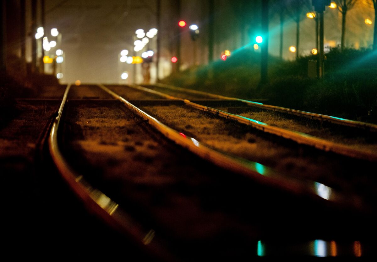 Empty rails near a subway station at night with lights in the distance.