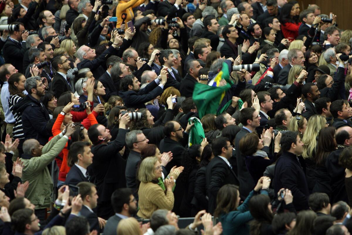 Members of media from around the world greet newly elected Pope Francis during an audience with journalists inside the Paul VI hall on Saturday in Vatican City. In the center is a person draped in the green, yellow and blue Brazilian flag.