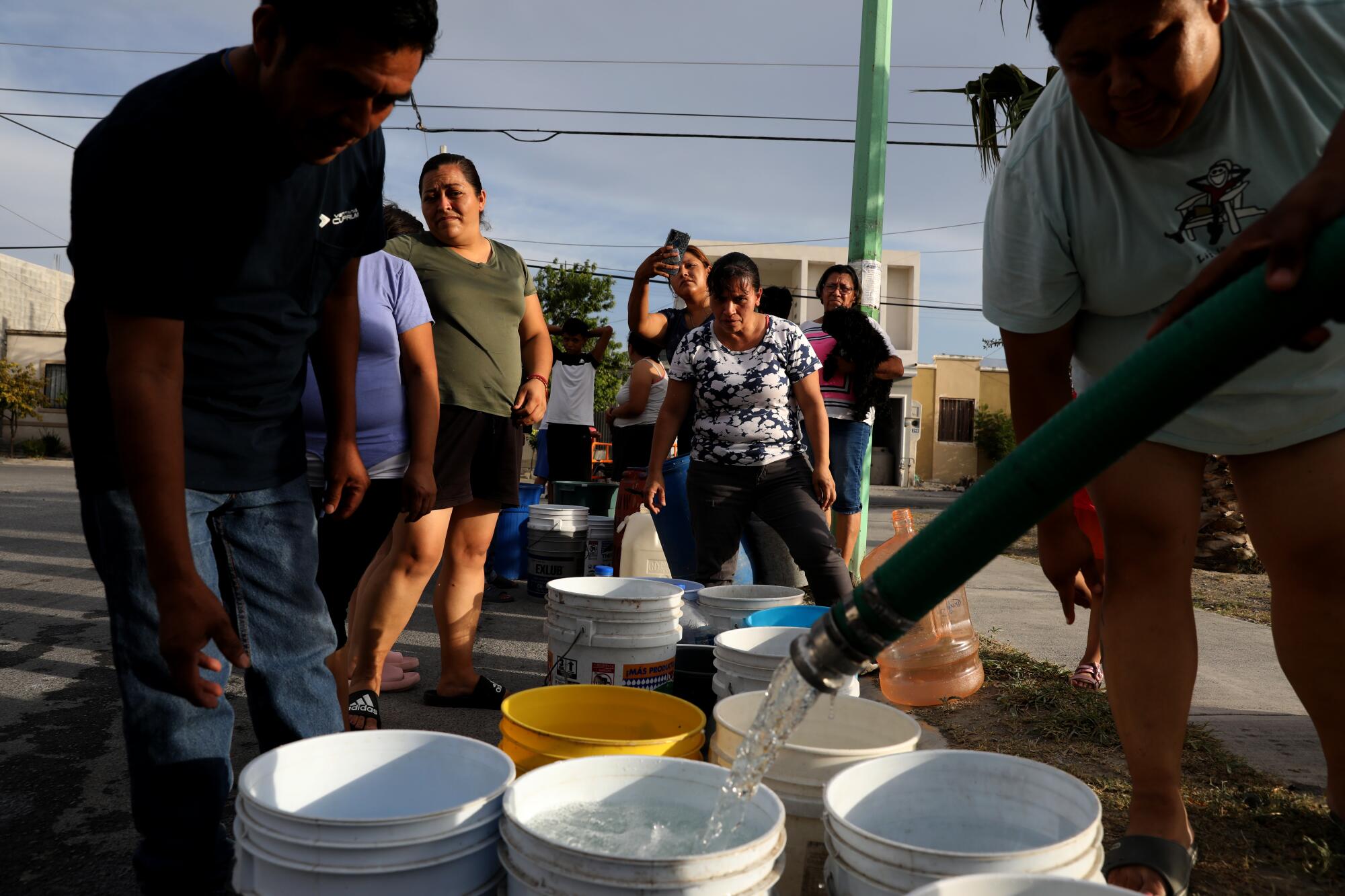 Water from a hose fills a bucket as people wait in line