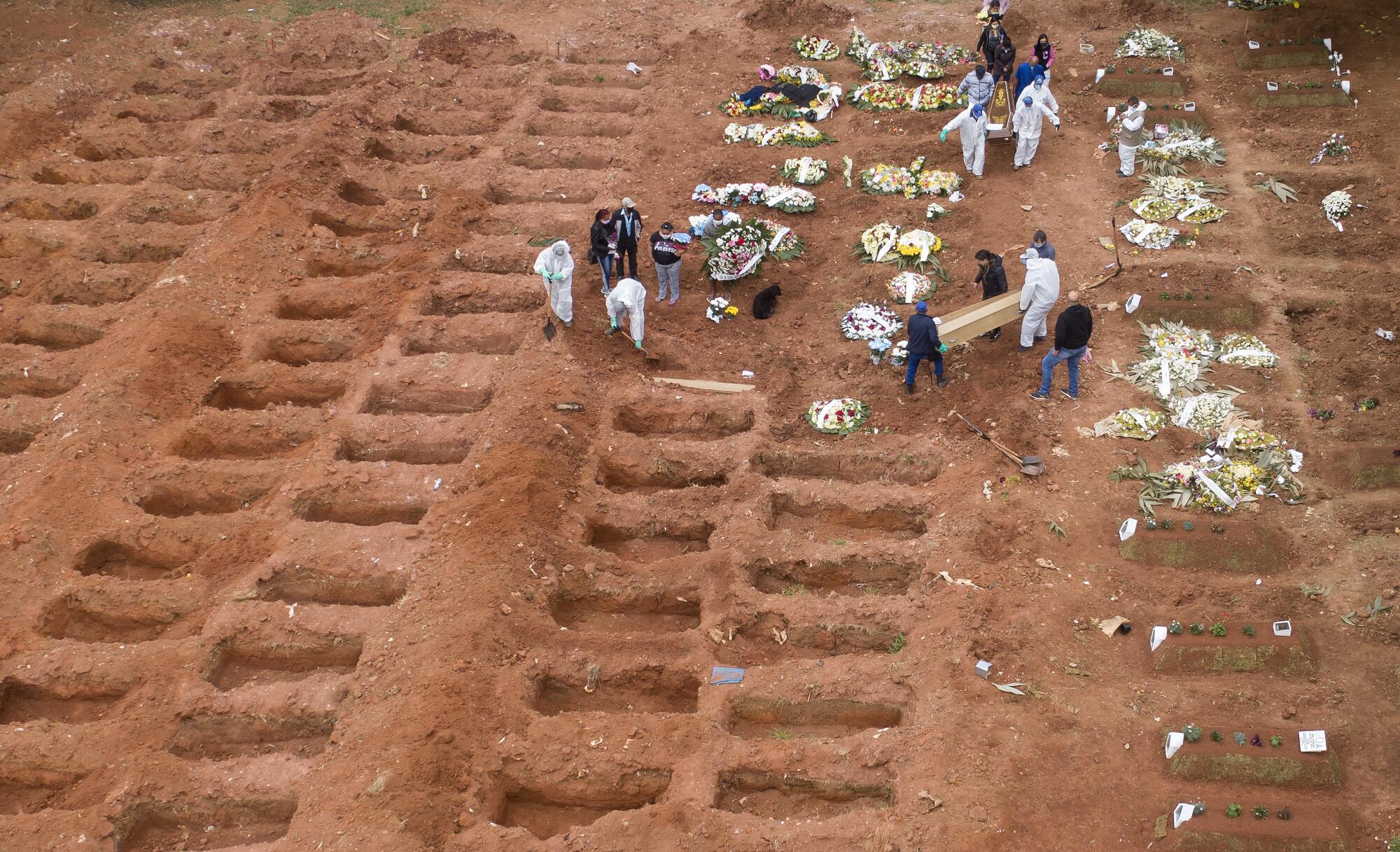 Workers in protective clothing bury three victims of COVID-19 at a cemetery.