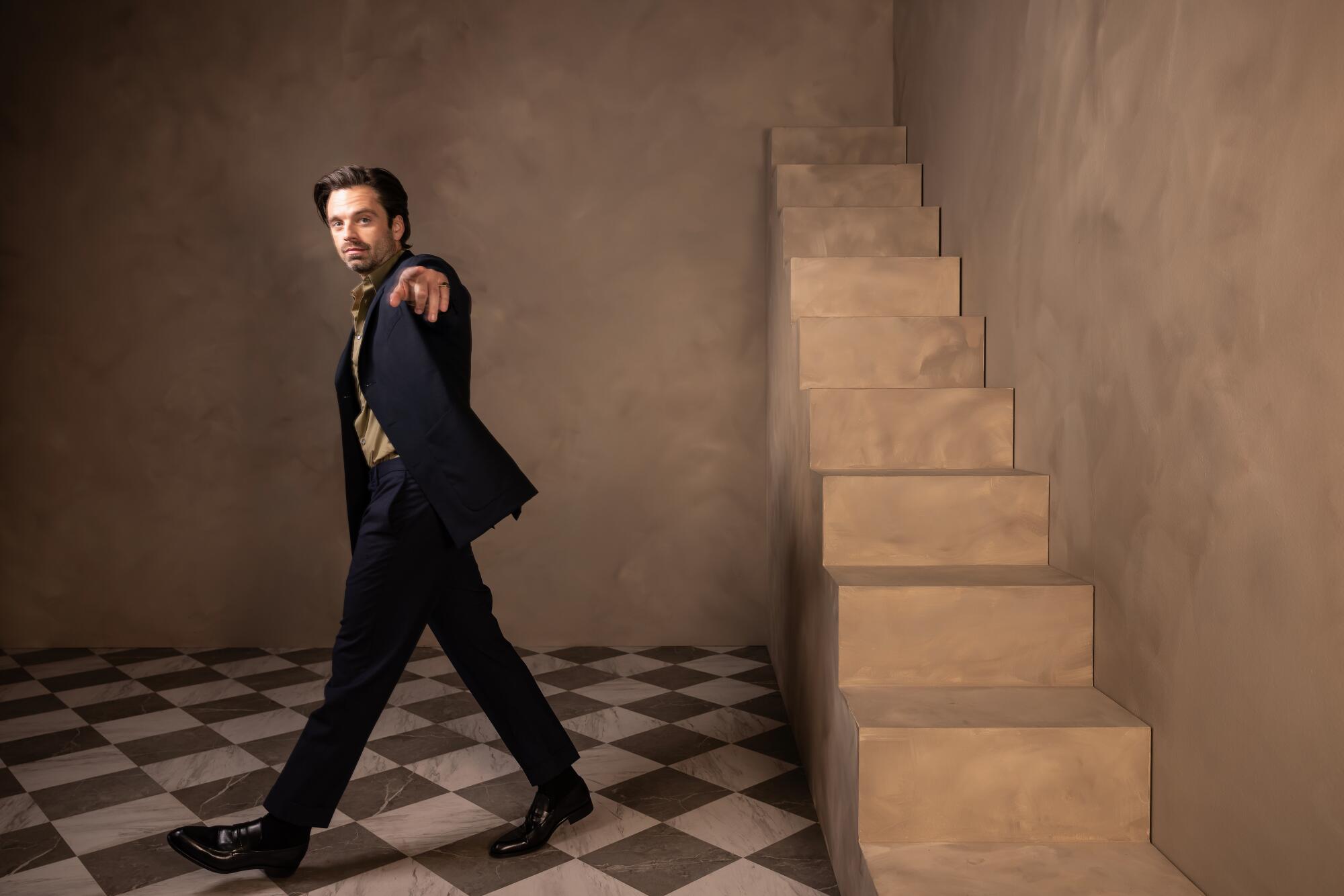 Sebastian Stan points at the camera as he walks for a portrait.