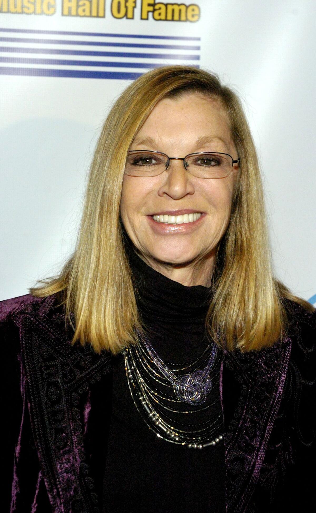 A woman with long brown hair and dressed in a black suit smiles.