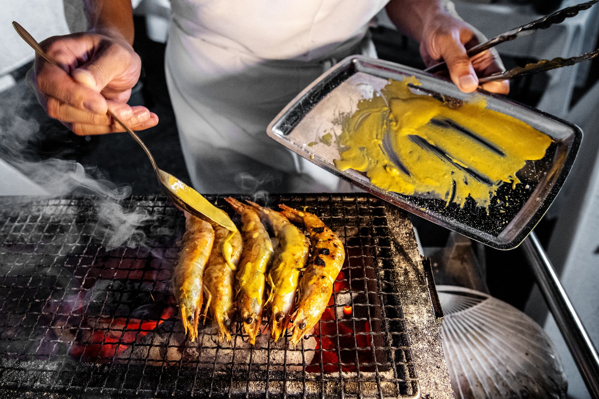 A chef brushes sauce on large prawns on a grill