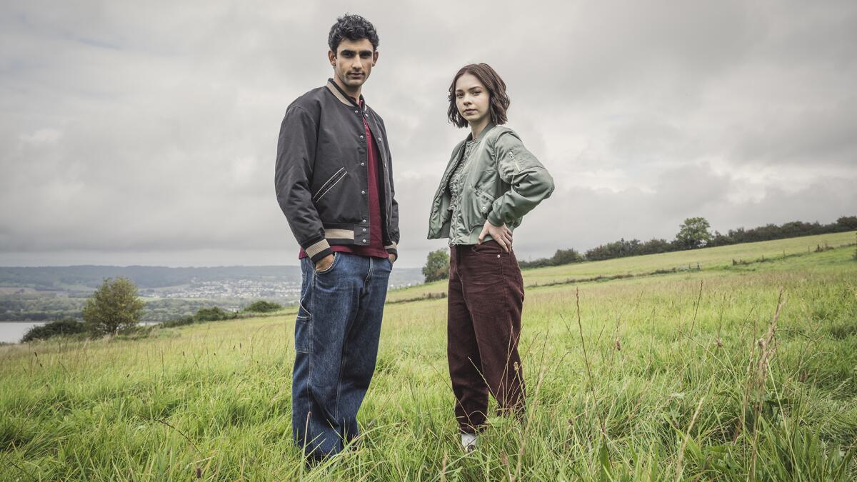 A teenage boy and girl standing a green, grassy field.