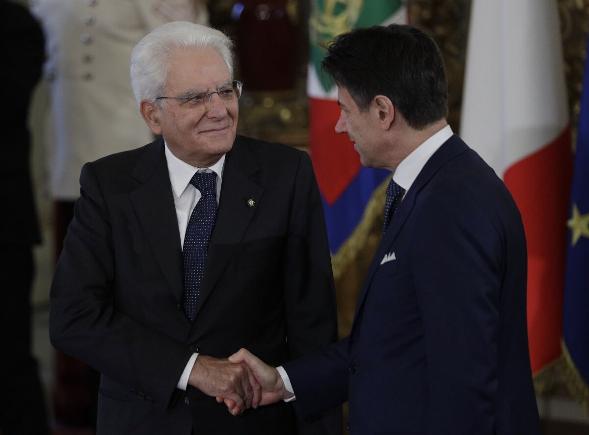 Sergio Mattarella shakes hands with Giuseppe Conte, with national flags in the background.