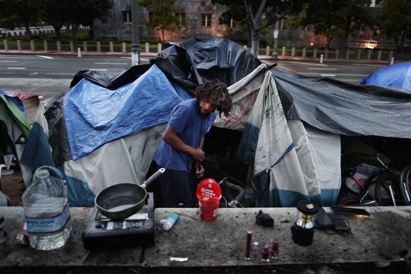 LOS ANGELES, CA - JANUARY 17, 2022: Homeless for six years, Dante Nesbit, 31, sweeps the area outside his tent at a homeless encampment on the sidewalk on Main Street January 17, 2022 in Los Angeles, California. Mayoral candidate Karen Bass wants to convert the vacant St. Vincent Medical Center near downtown into a housing facility for the homeless.(Gina Ferazzi / Los Angeles Times)