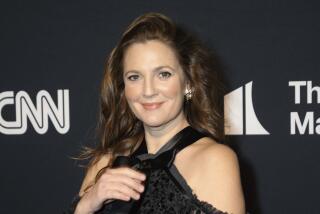 Drew Barrymore poses in a black, lacy dress in front of a black backdrop.