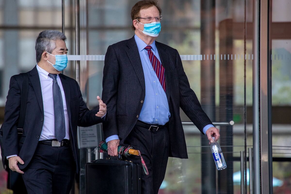 Two men in suits and surgical masks walking past glass doors