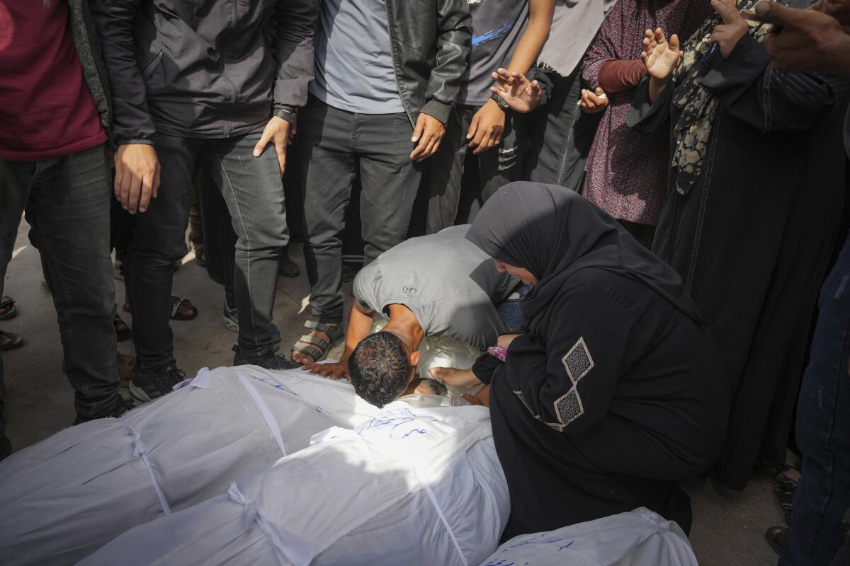 Palestinians stand and kneel near bodies of relatives wrapped in white cloth bags after an Israeli airstrike.